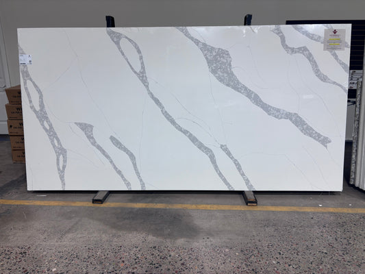 Alabama quartz slab standing in the Marbino Surfaces warehouse, bright white with bold diagonal gray veins